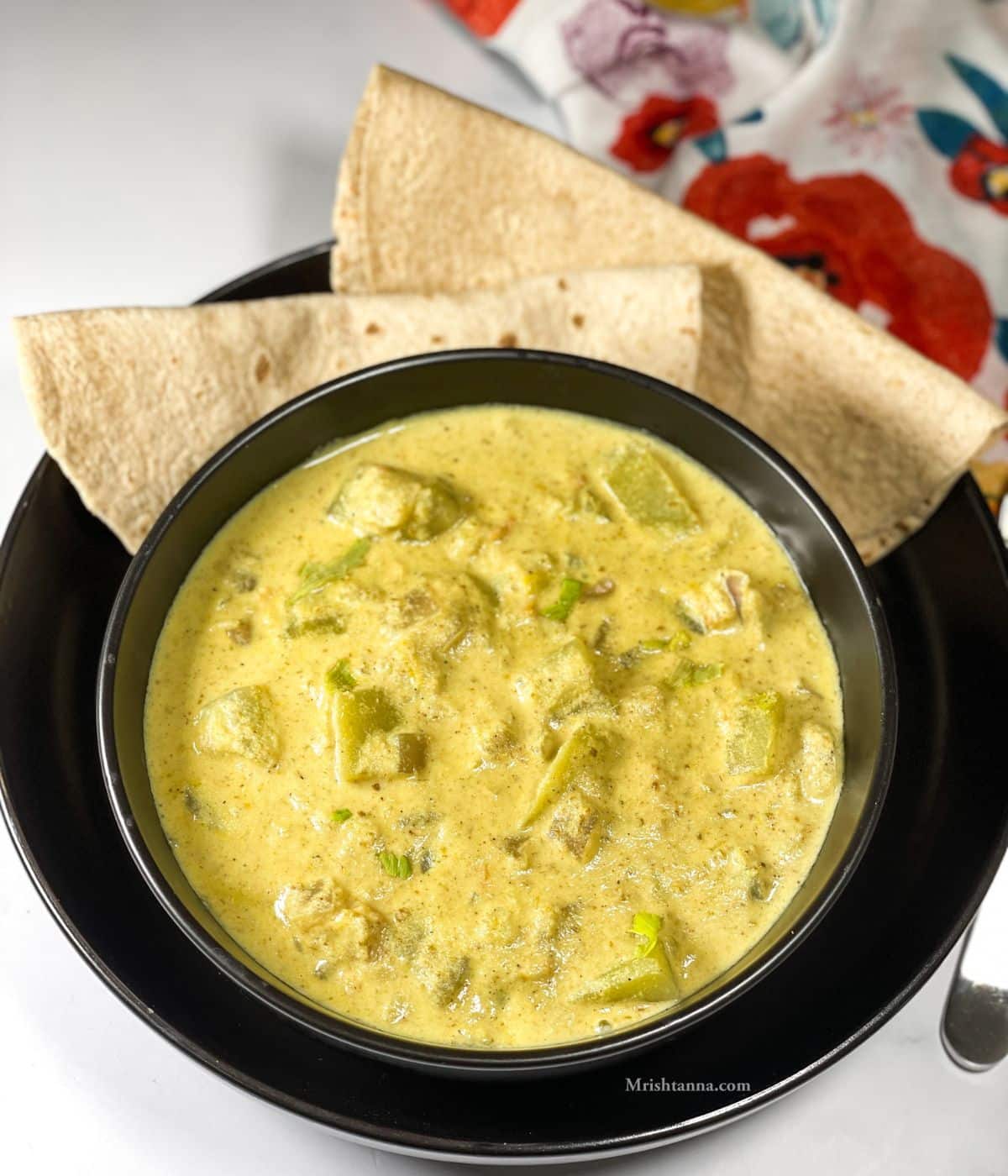 A bowl of bottle gourd kurma is on the plate with rotis.
