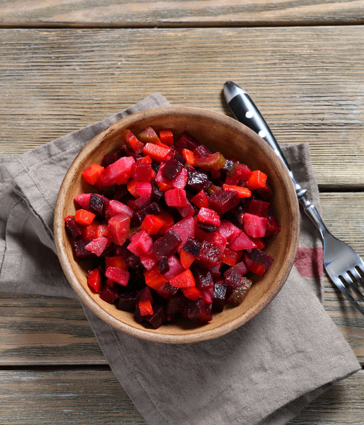 A bowl of beet salad on the  cloth napkin with two forks.