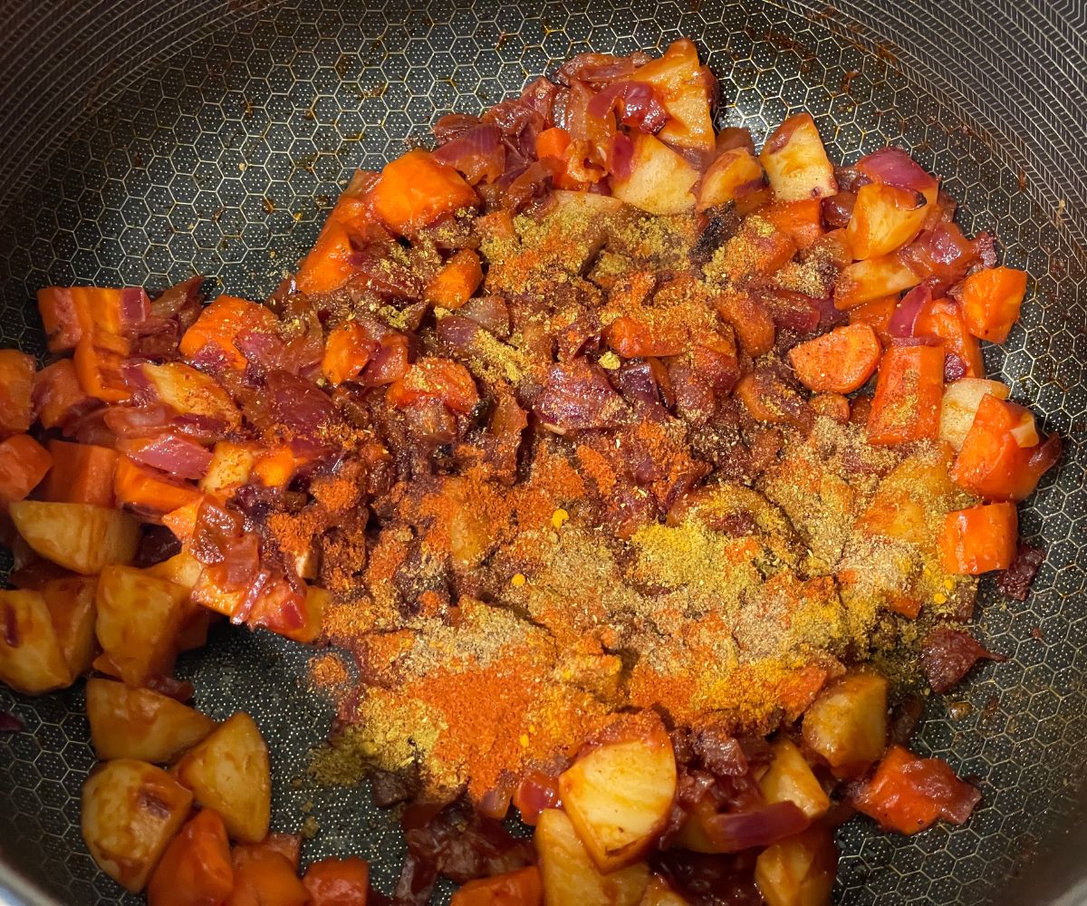 A pan is with veggies and spices over the heat.