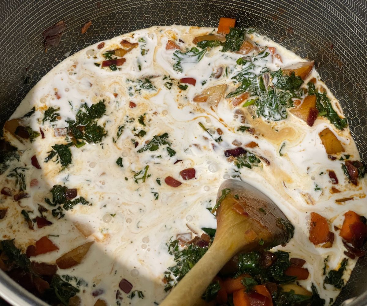 A pot is with kale, veggies and coconut milk over the stove top.