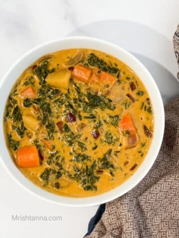 A bowl of kale curry is on the table with a cloth by the side.