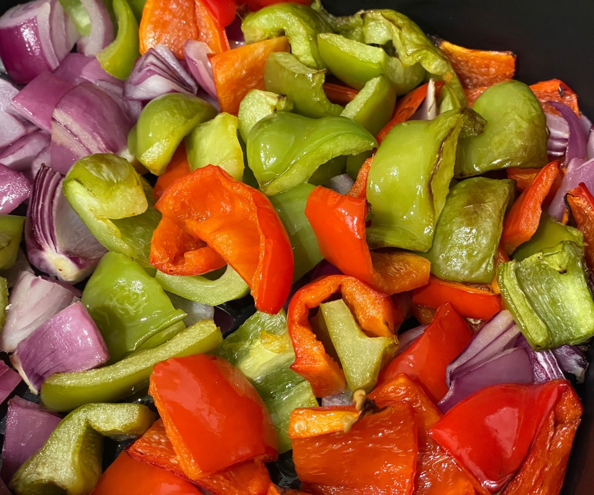 Air fryer basket is filled with fried bell peppers and onions.