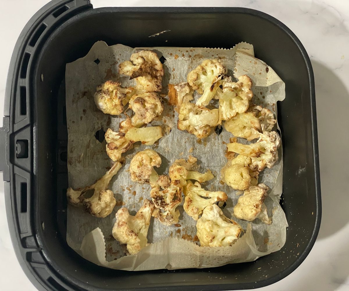 Air fryer basket with air fried cauliflower florets.