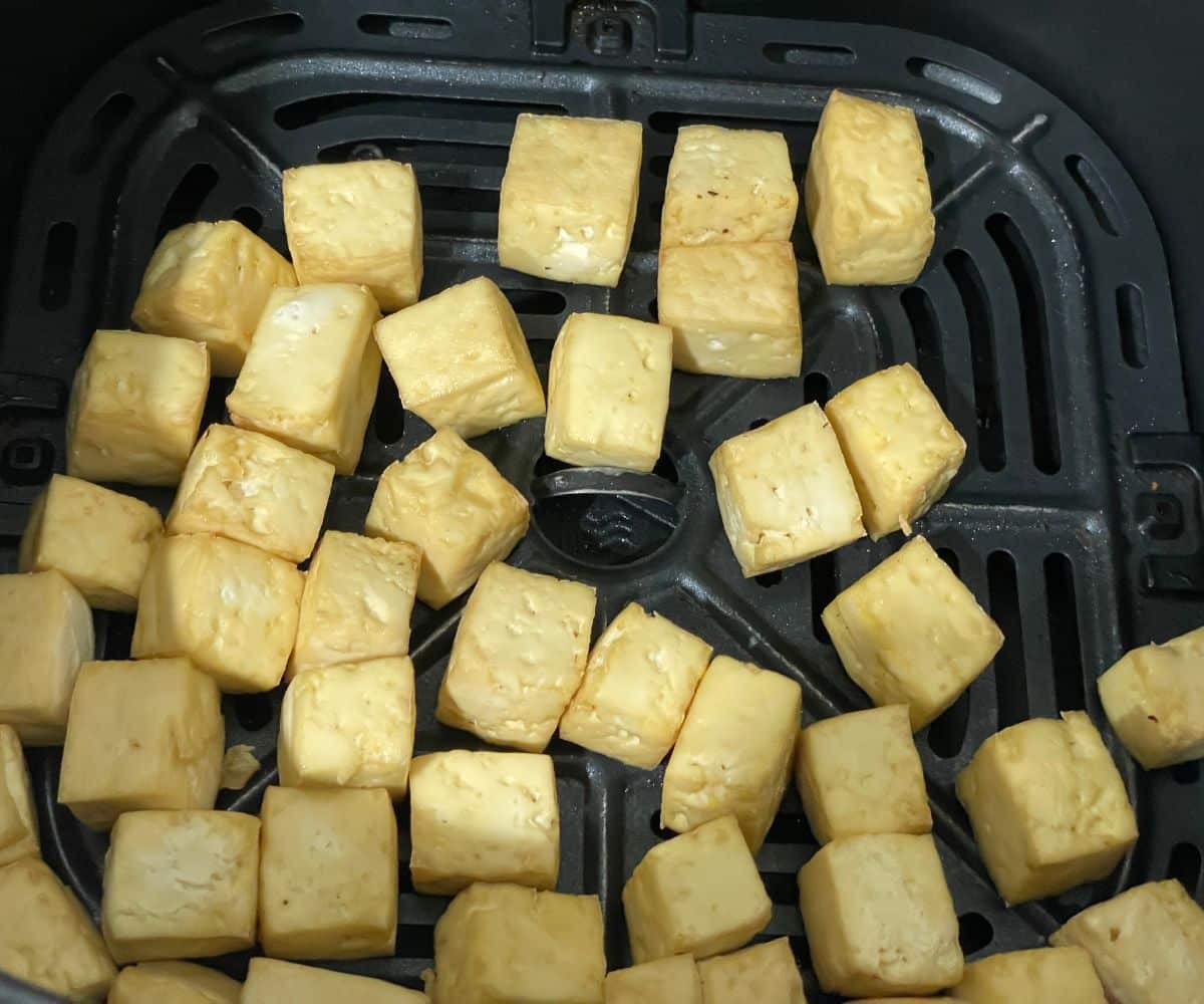 Air fryer basket is with fried tofu cubes.