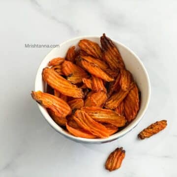 A bowl is filled with air fried carrot chips.