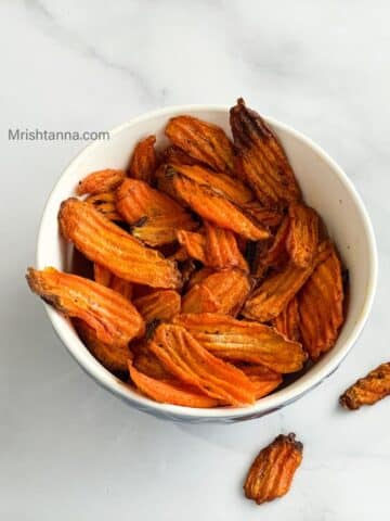 A bowl is filled with air fried carrot chips.