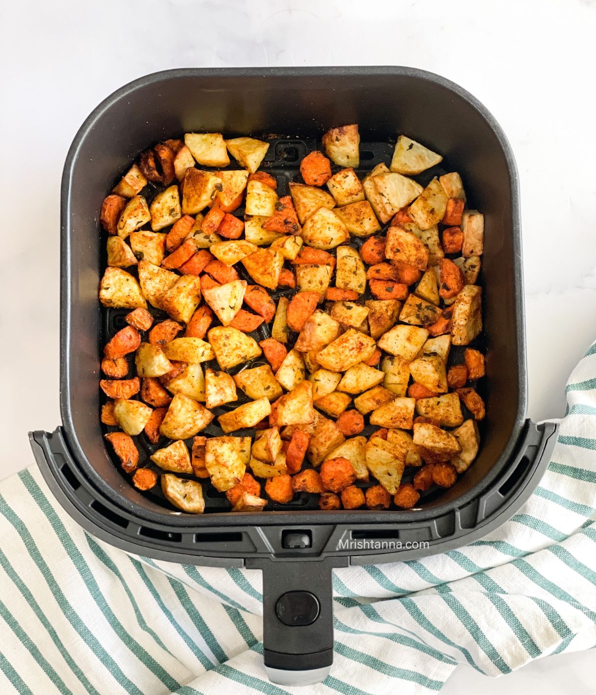 The air fryer basket is with roasted carrots and potatoes over the napkin.