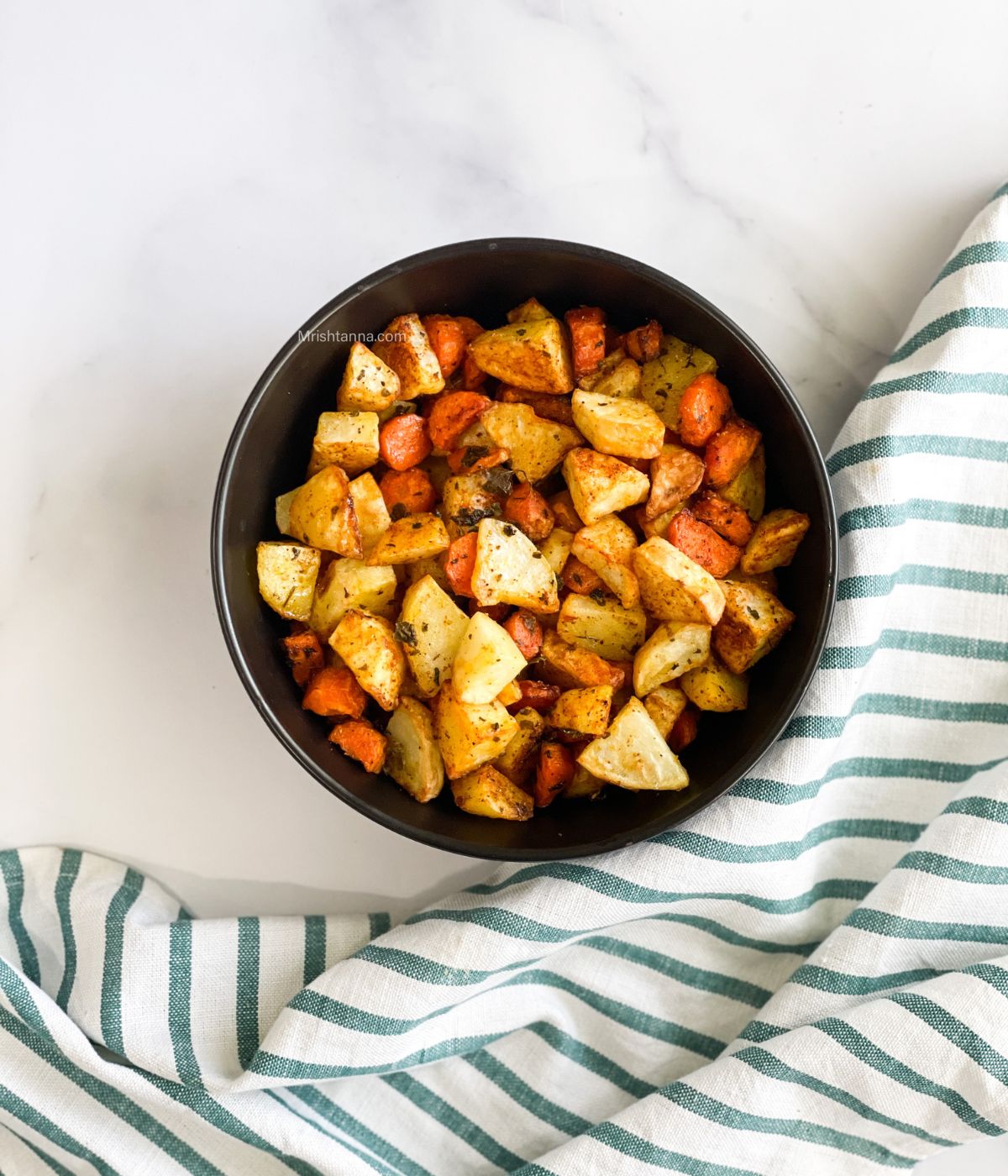 A bowl of air fryer roasted carrots and potatoes on the table.