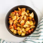 A bowl of roasted carrots and potatoes are on the table.