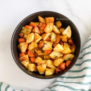 A bowl of roasted carrots and potatoes are on the table.