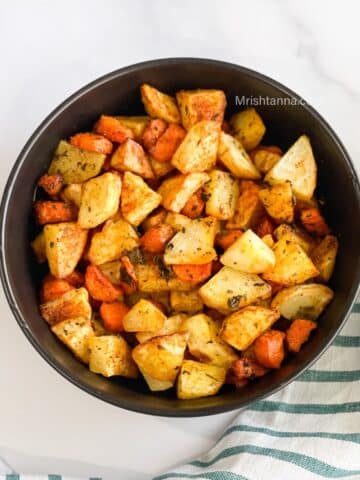 A bowl of roasted carrots and potatoes are on the table.