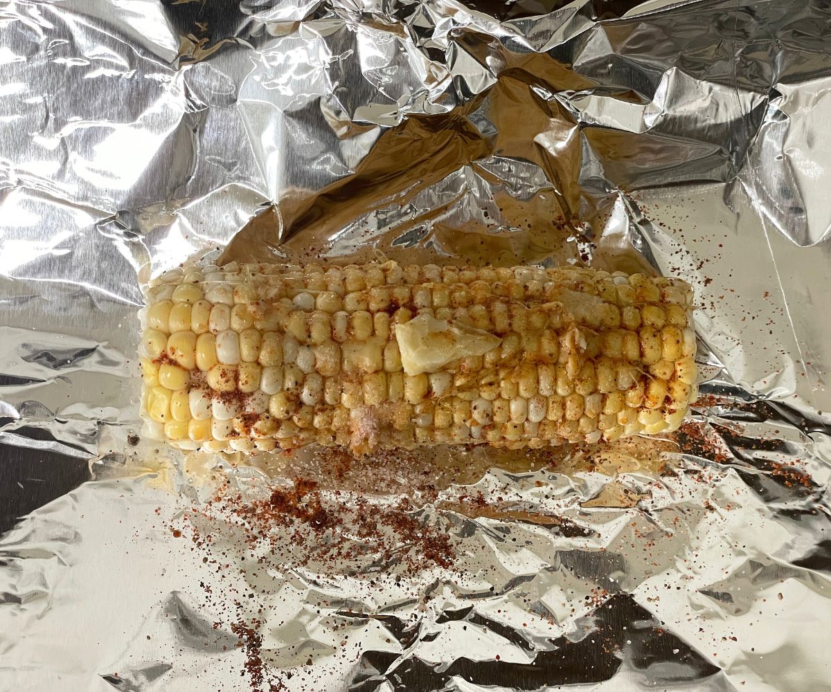 The corn on the cob is covered with butter and spices on the foil.