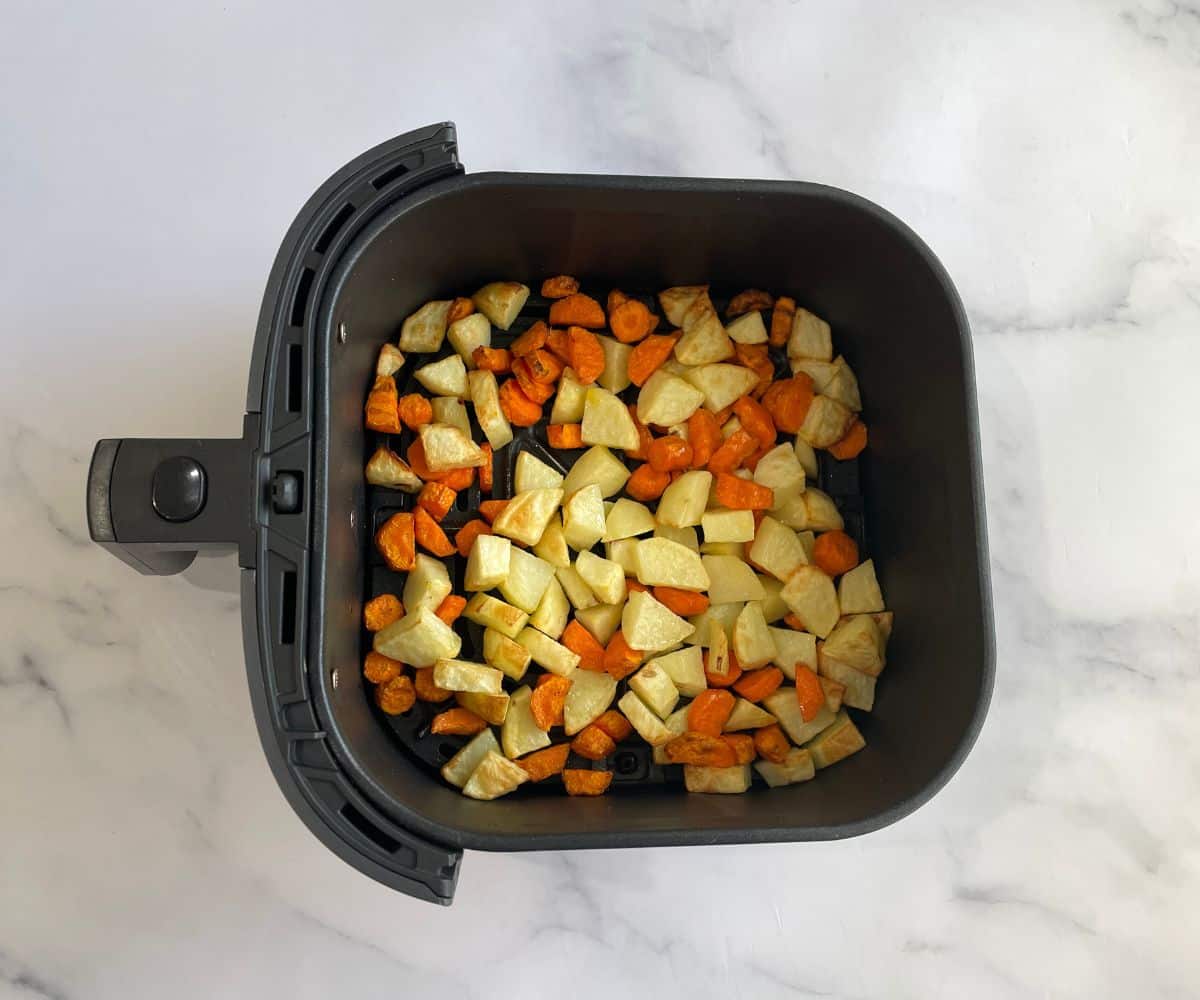 Air fryer basket is with carrots and potatoes.