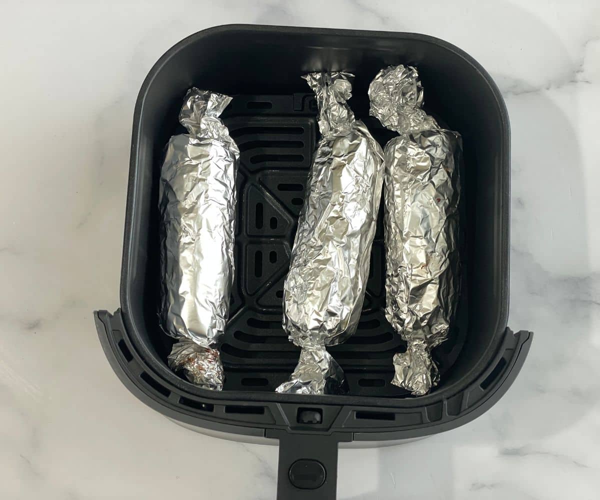 Air fryer basket is with corn on the cob in foil.