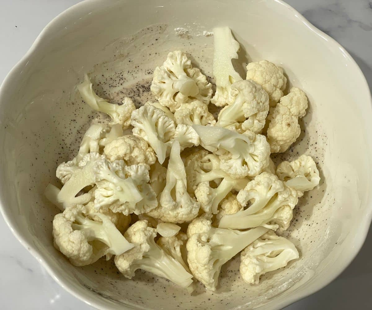 A bowl is with flour mixture and cauliflower florets.