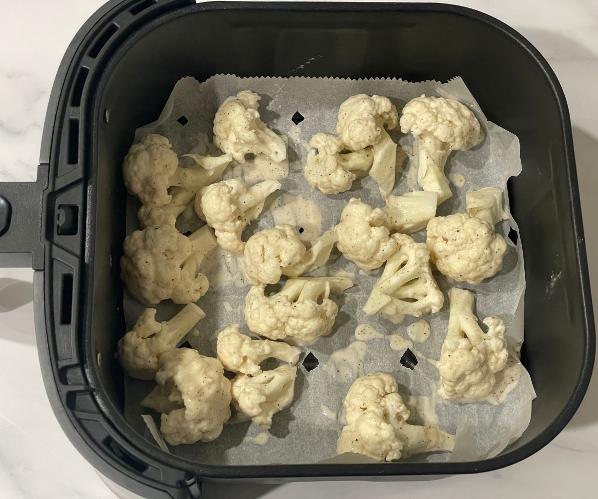 The air fryer basket is with batter coated cauliflower florets.