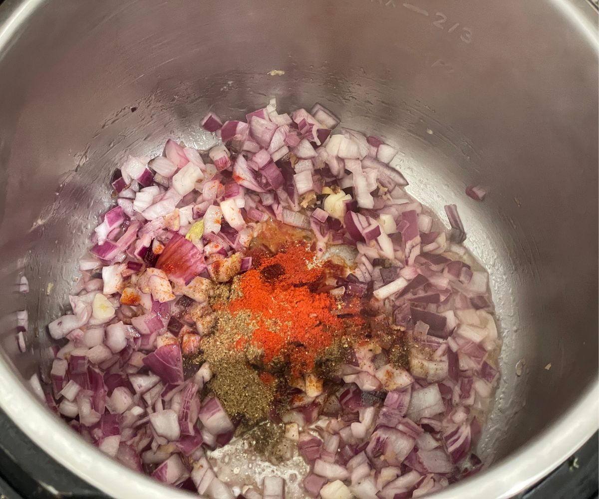 An instant pot is with spices and chopped onions on saute mode.