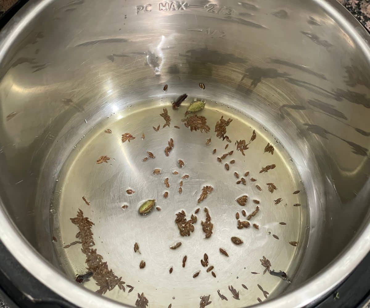 An instant pot is with cumin seeds and oil.
