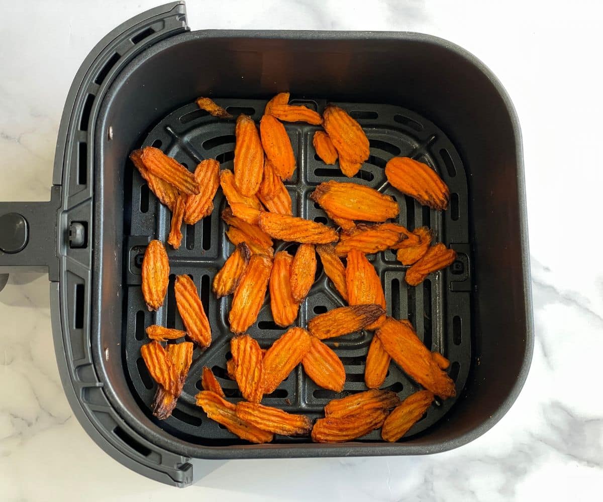 Air fryer basket with fried carrot chips.