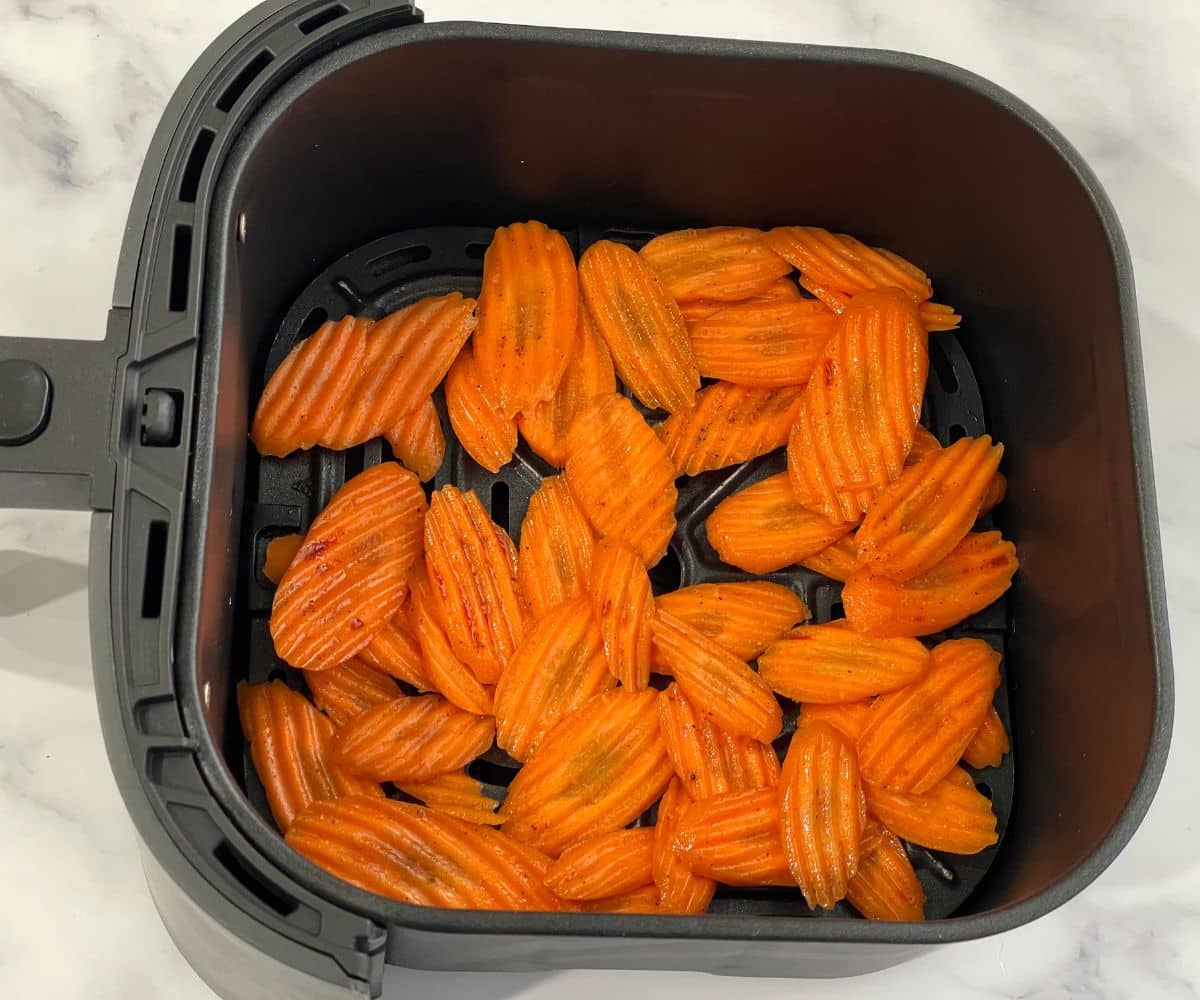 Air fryer basket is with raw carrot chips.