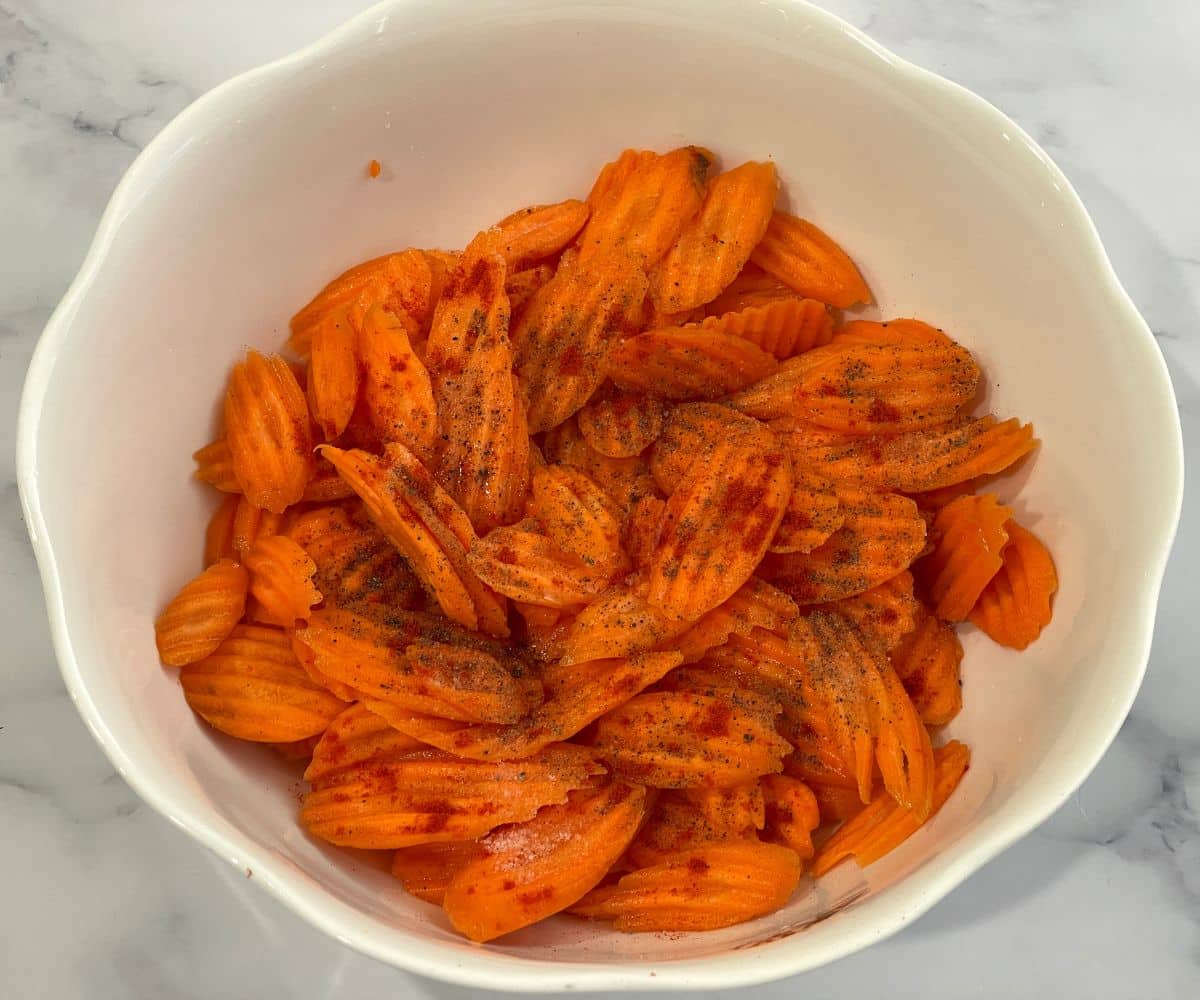 A big bowl is with seasoned carrot slices.