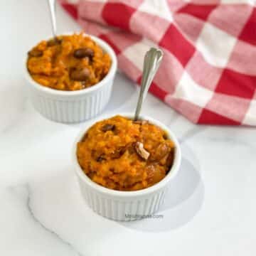 A bowl of carrot halwa is with a spoon inserted.