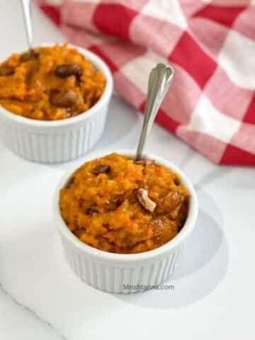 A bowl of carrot halwa is with a spoon inserted.