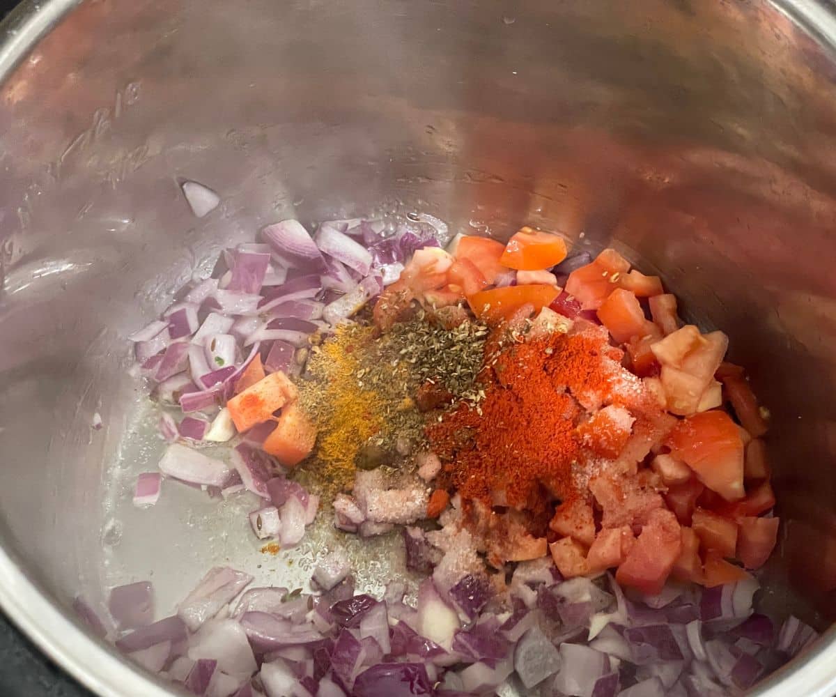 An instant pot is with onion, tomatoes and spices.