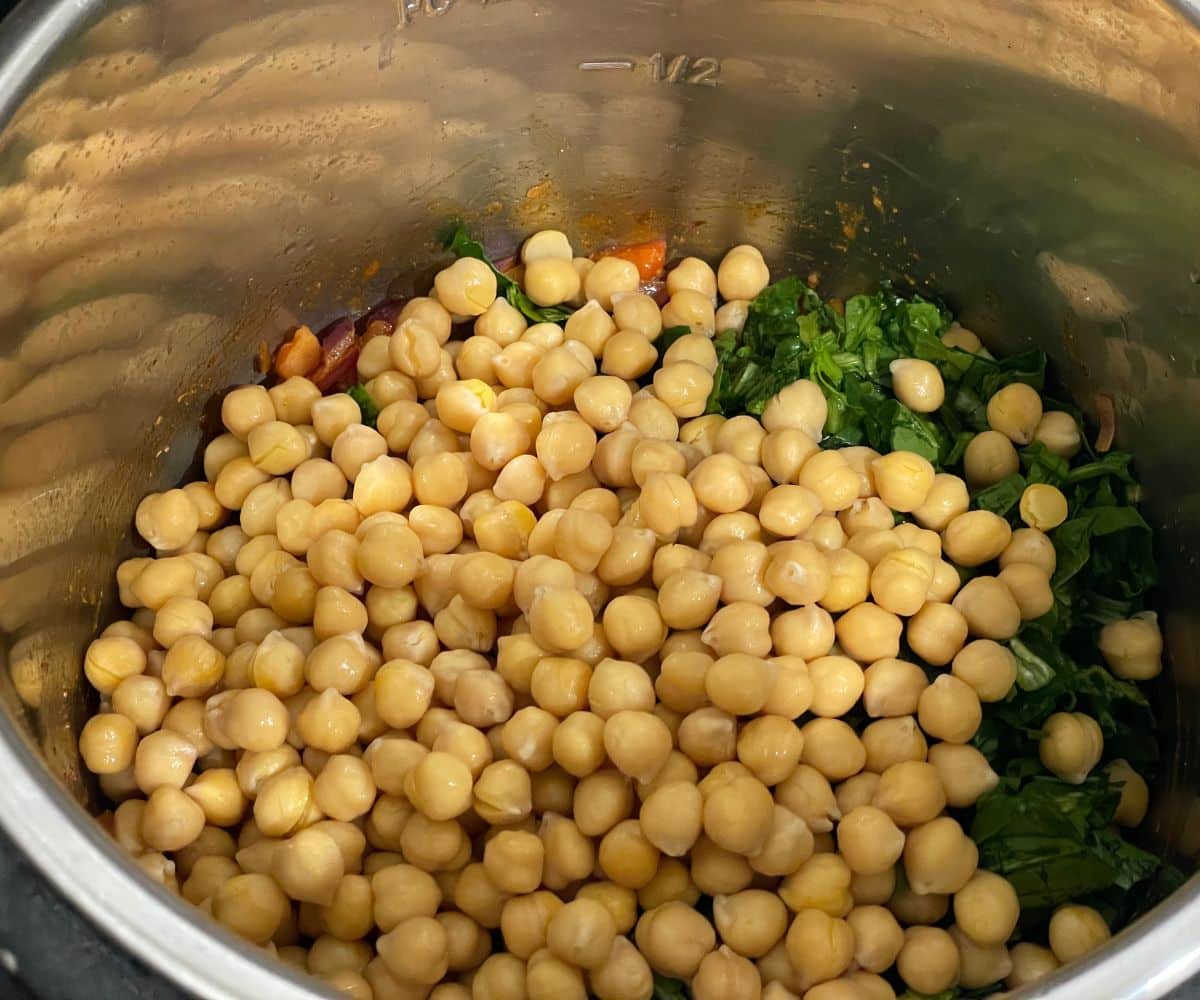 An instant pot is with chickpeas and spinach on saute mode.