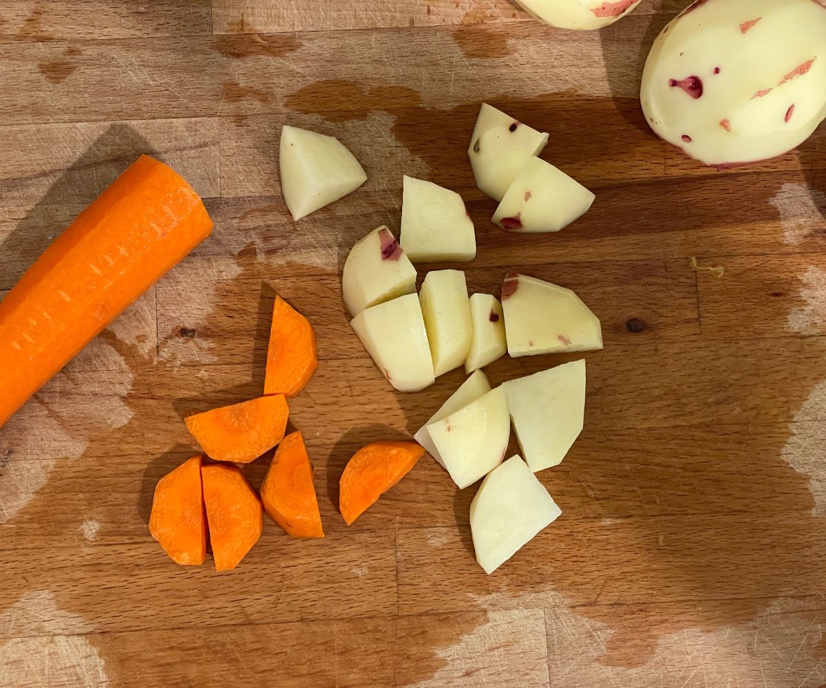 A cutting board is with chopped carrots and  potatoes.