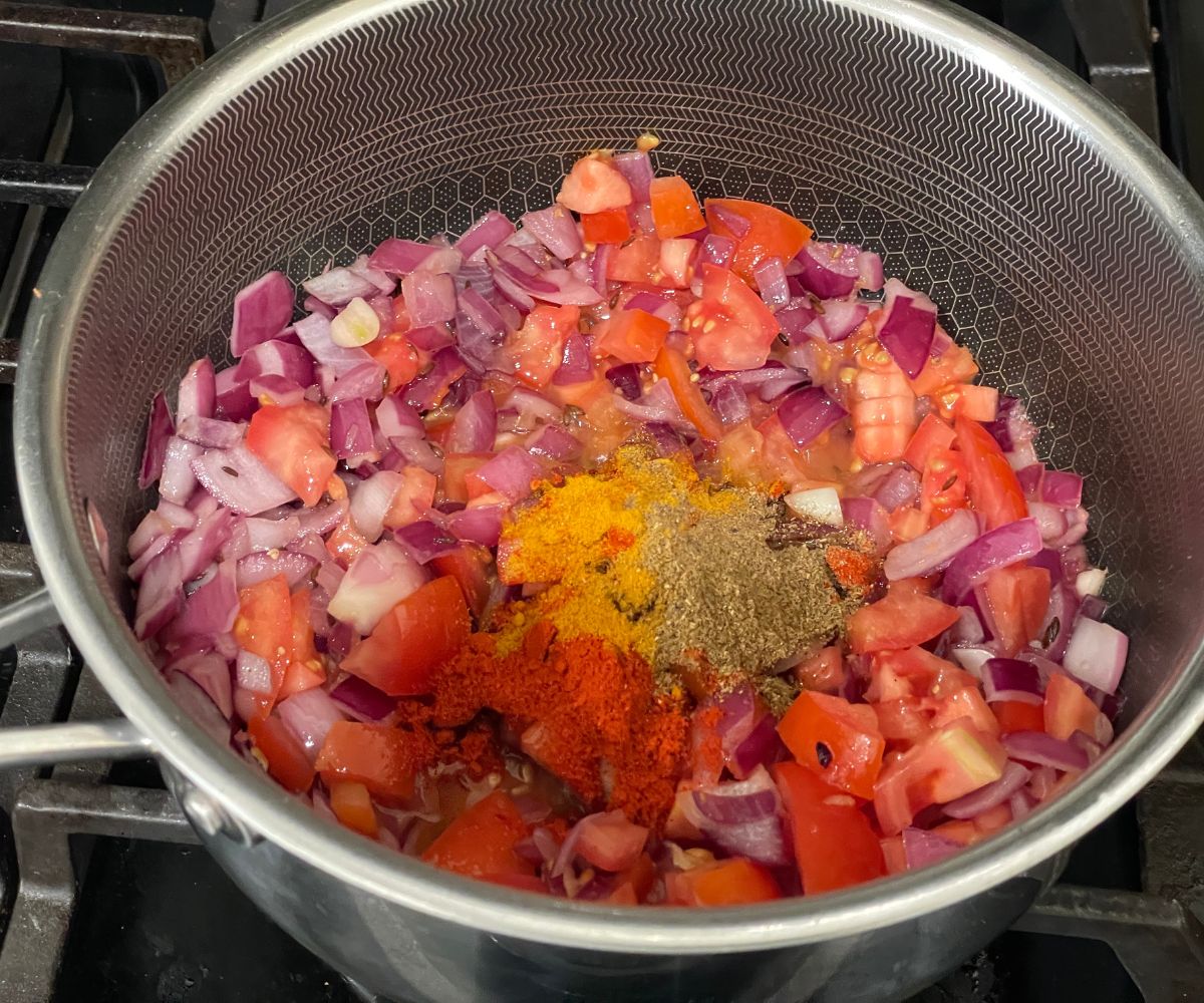 A pan is with vegetables and spices over the heat.