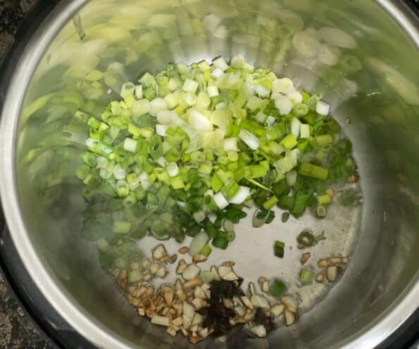 An instant pot is with scallions and garlic on saute mode.