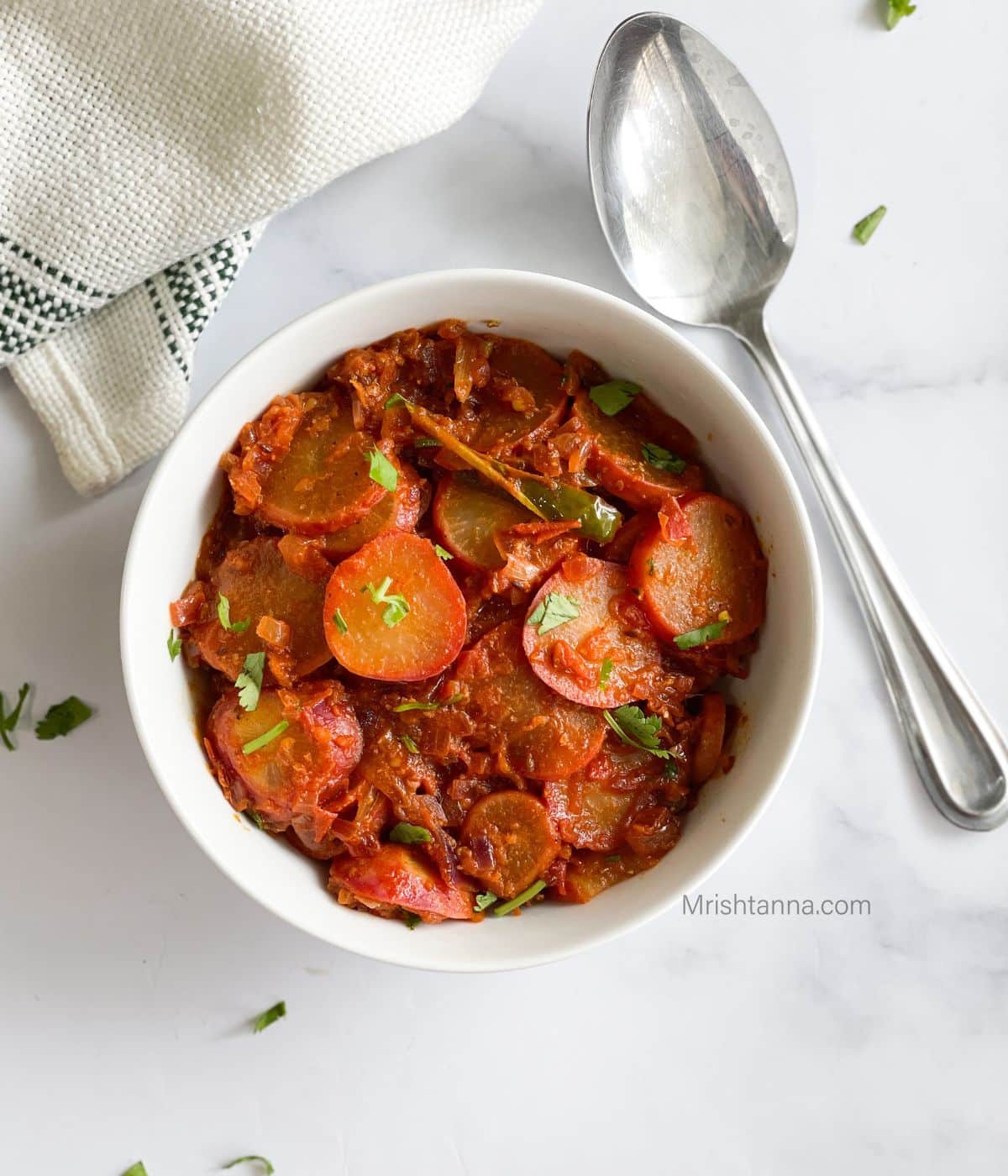 A bowl of Indian radish curry is on the table with a spoon.