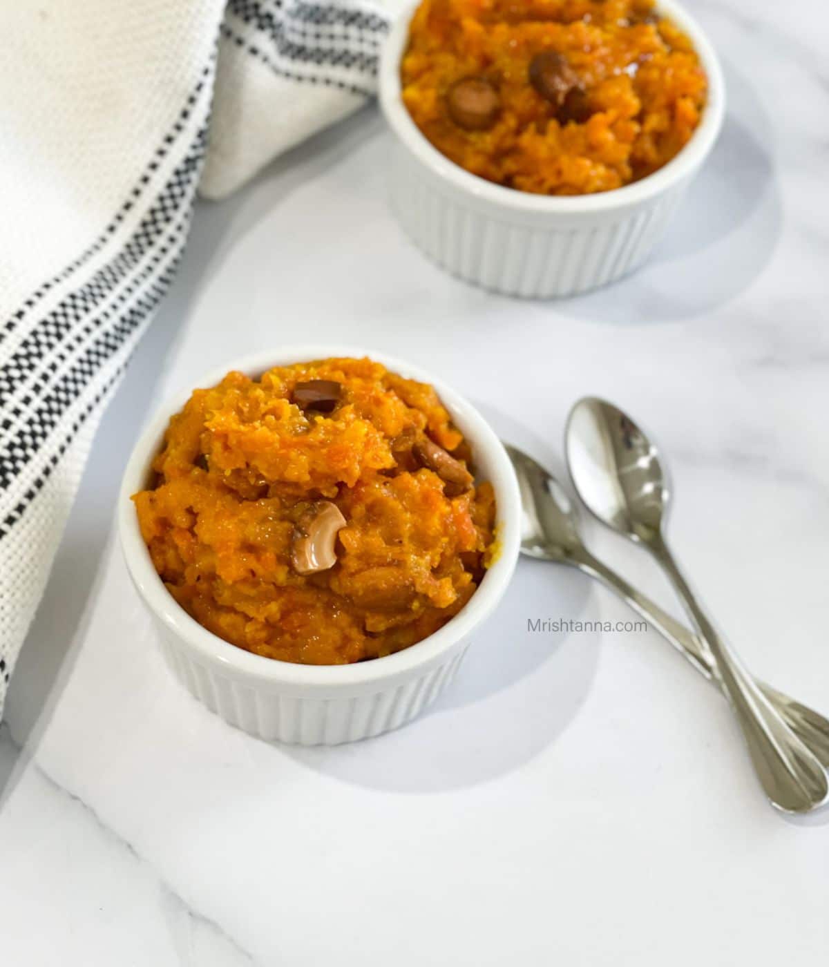 Two bowls are with vegan carrot halwa on the table with spoons.