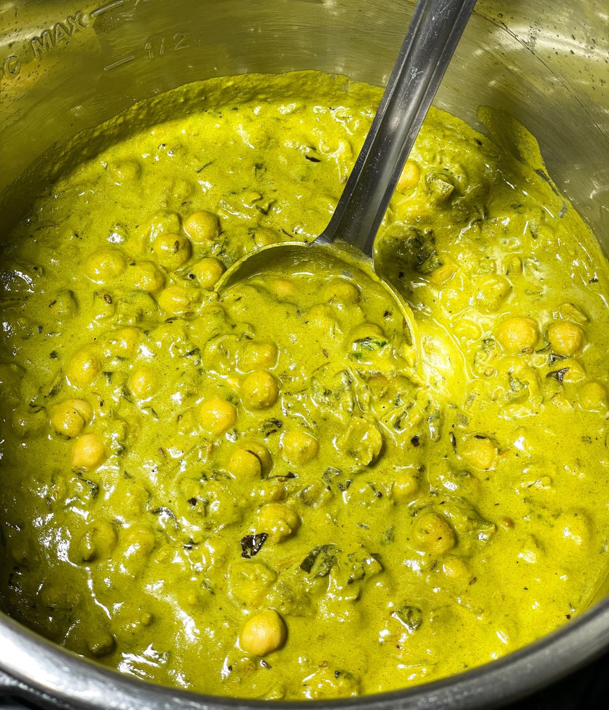 Chana palak curry is on the Instant pot with a big spoon inside.