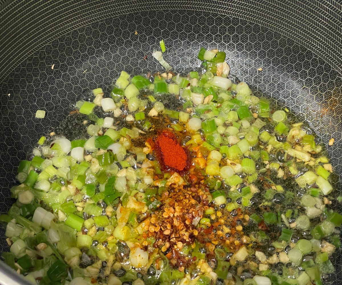 A pan is with spices and green onions over the heat.