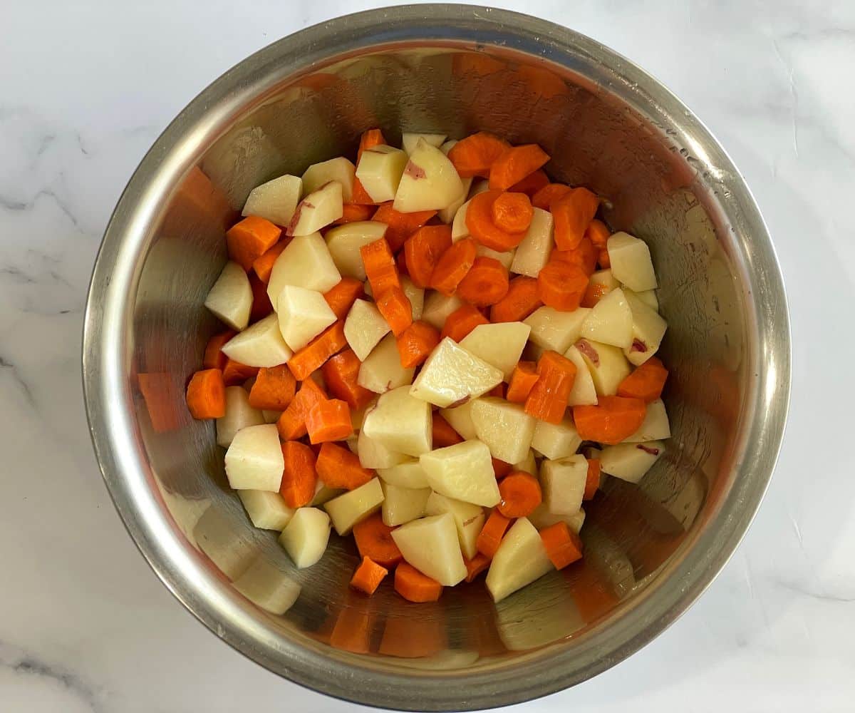 A bowl is with chopped carrots and potatoes.