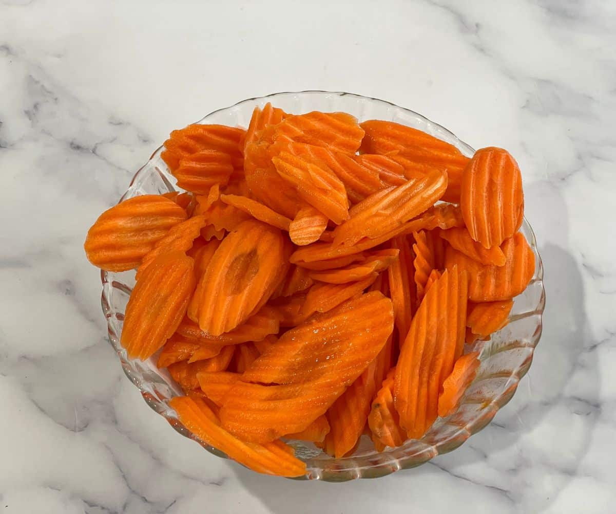 A bowl of raw carrot chips are on the table.