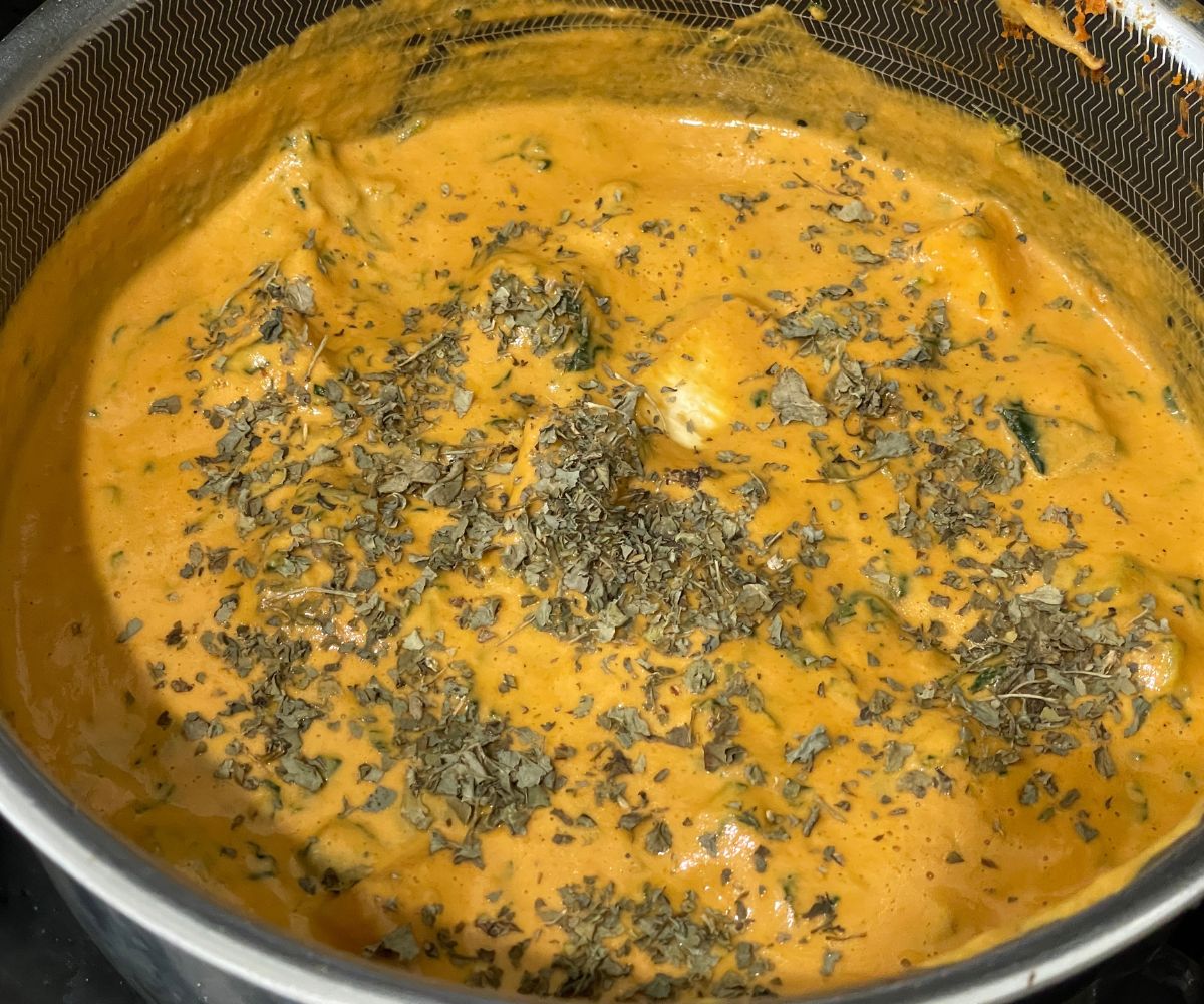 A pot of tofu curry is on the flame topped with kasuri methi.