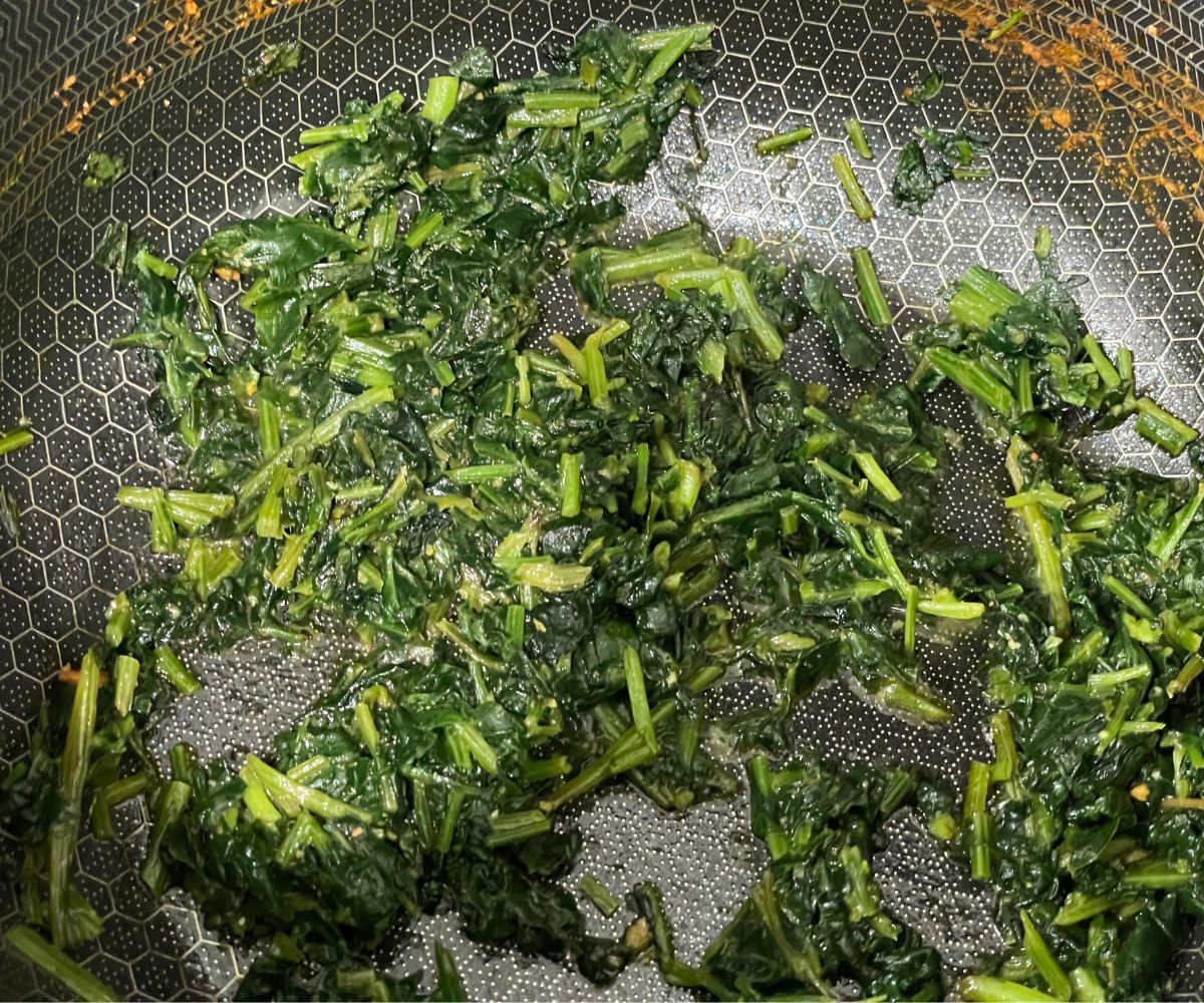 A pan is with chopped spinach over the flame.