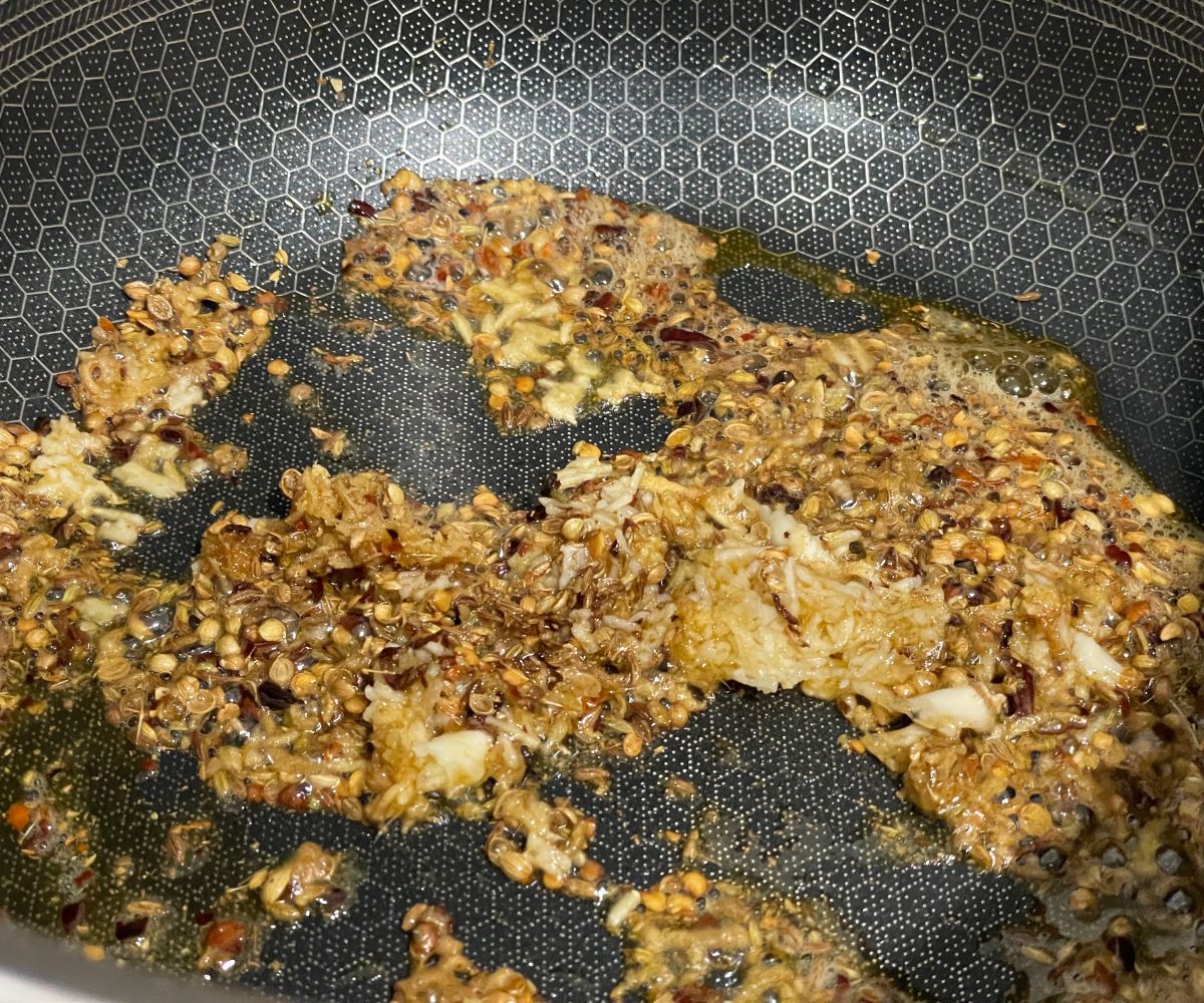 A heated pan is with crushed whole spices and ginger & garlic.