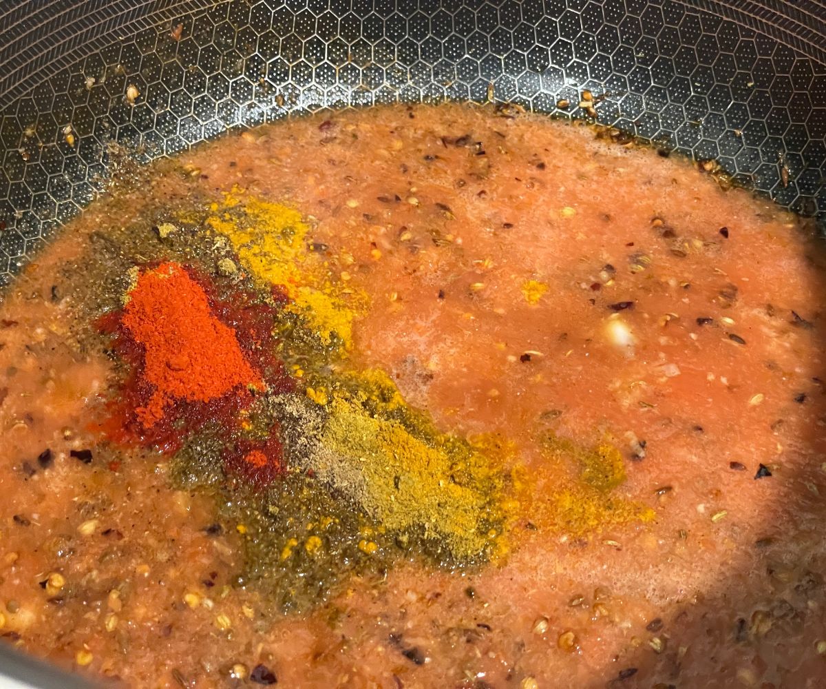 A heated pan is with tomato puree and spices.