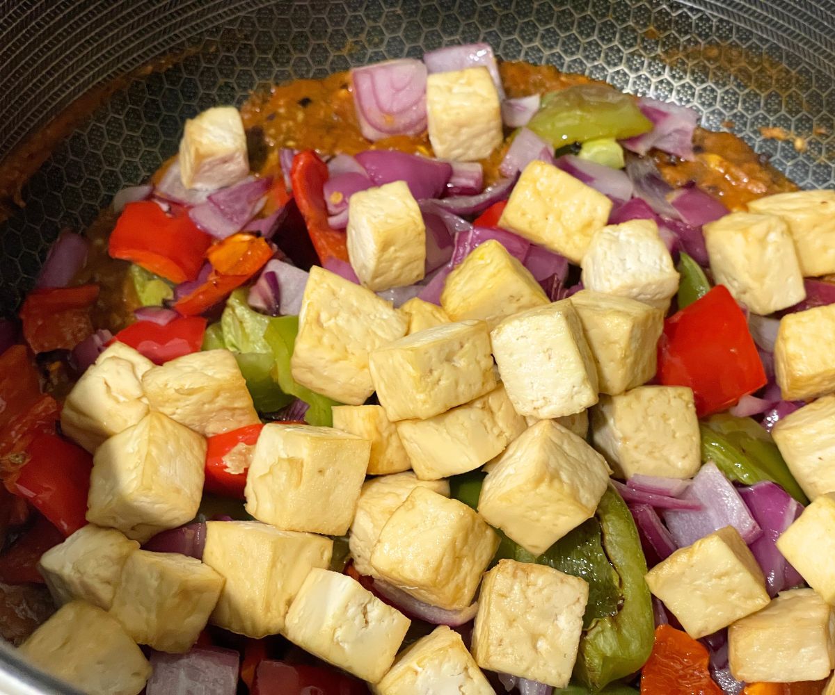A pan of tofu, bell peppers and spices over the flame.