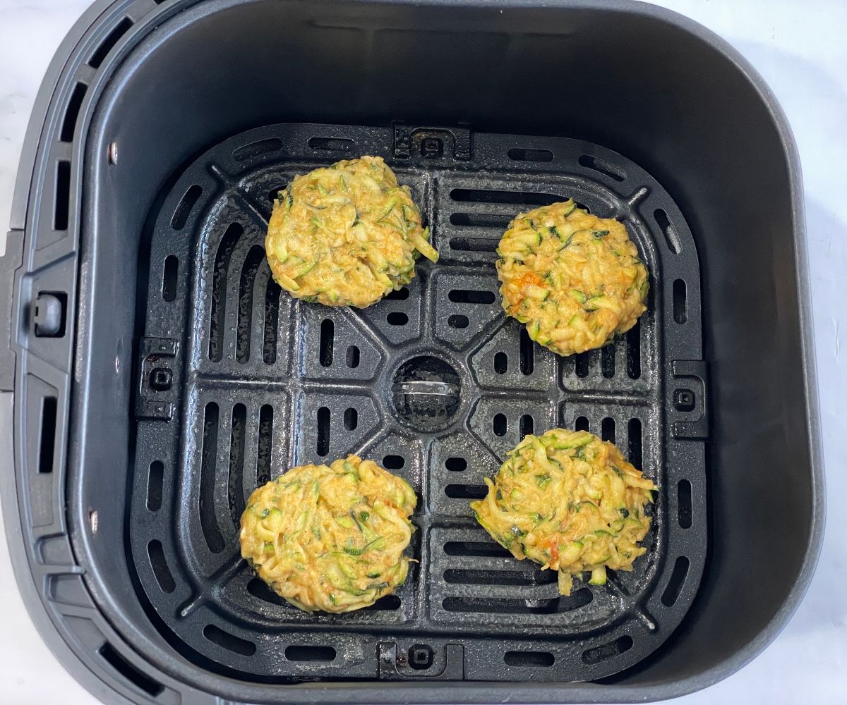 An air fryer basket is with zucchini fritter patties.