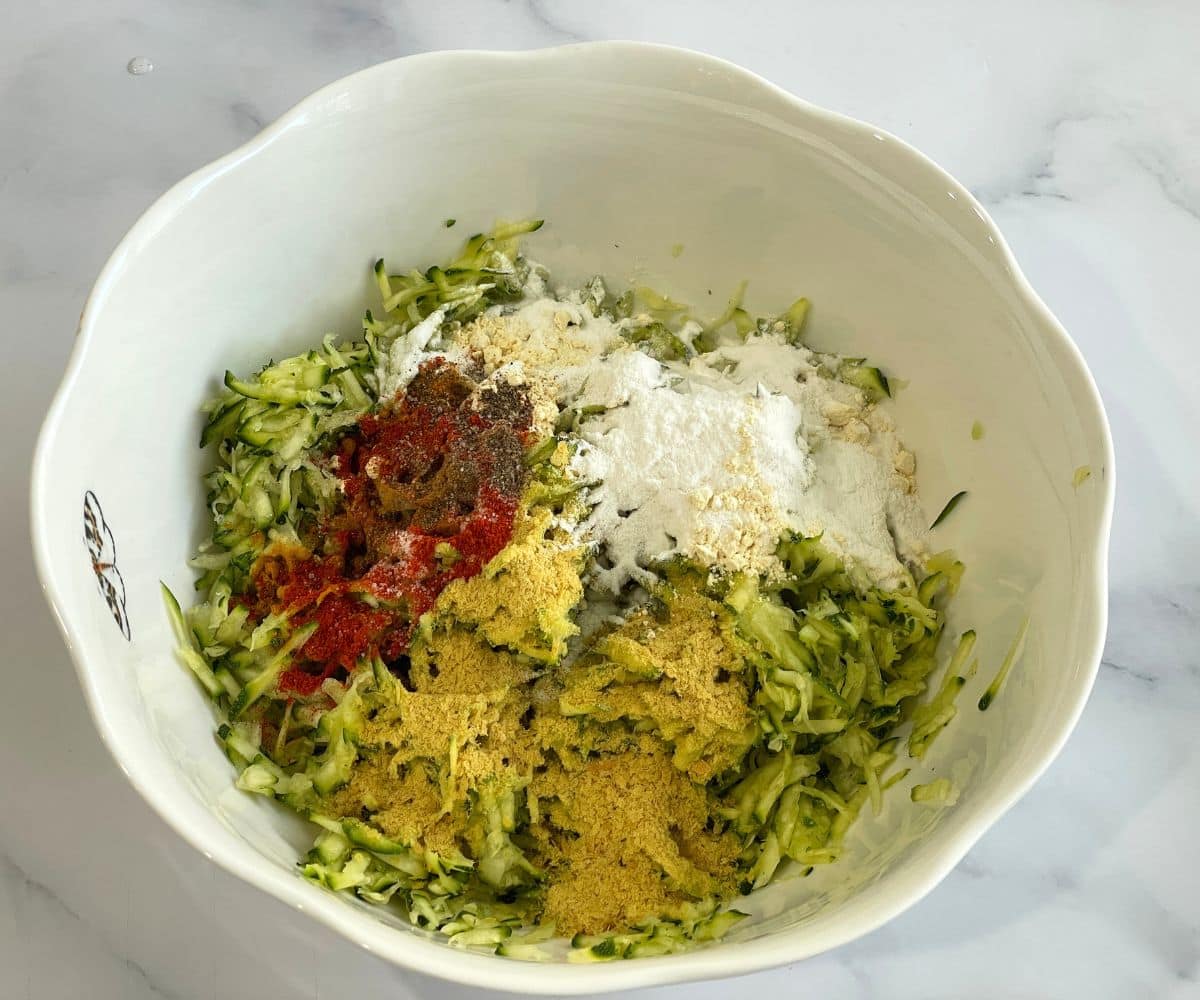 A bowl contains grated zucchini, flour and spices.