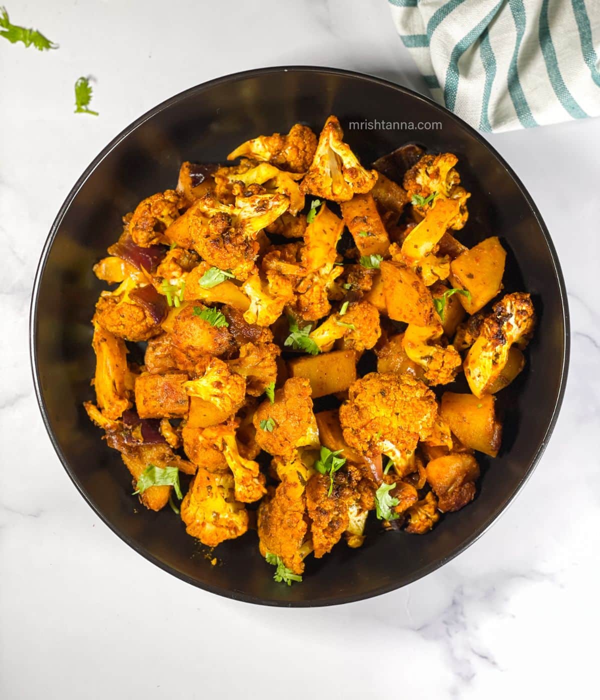 Air fryer aloo gobi is in the bowl topped with cilantro.