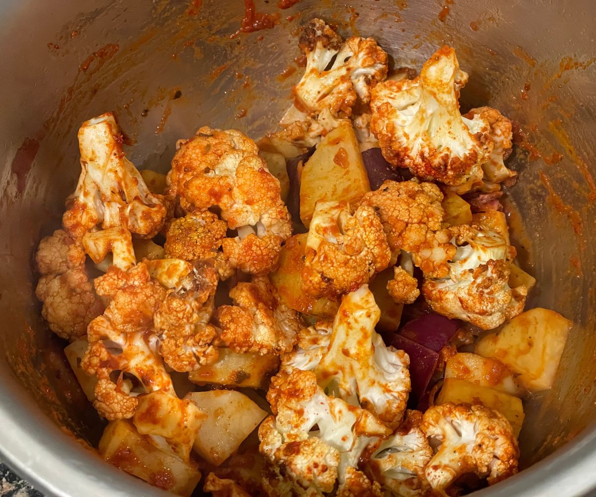 A bowl is with aloo gobi and spices.