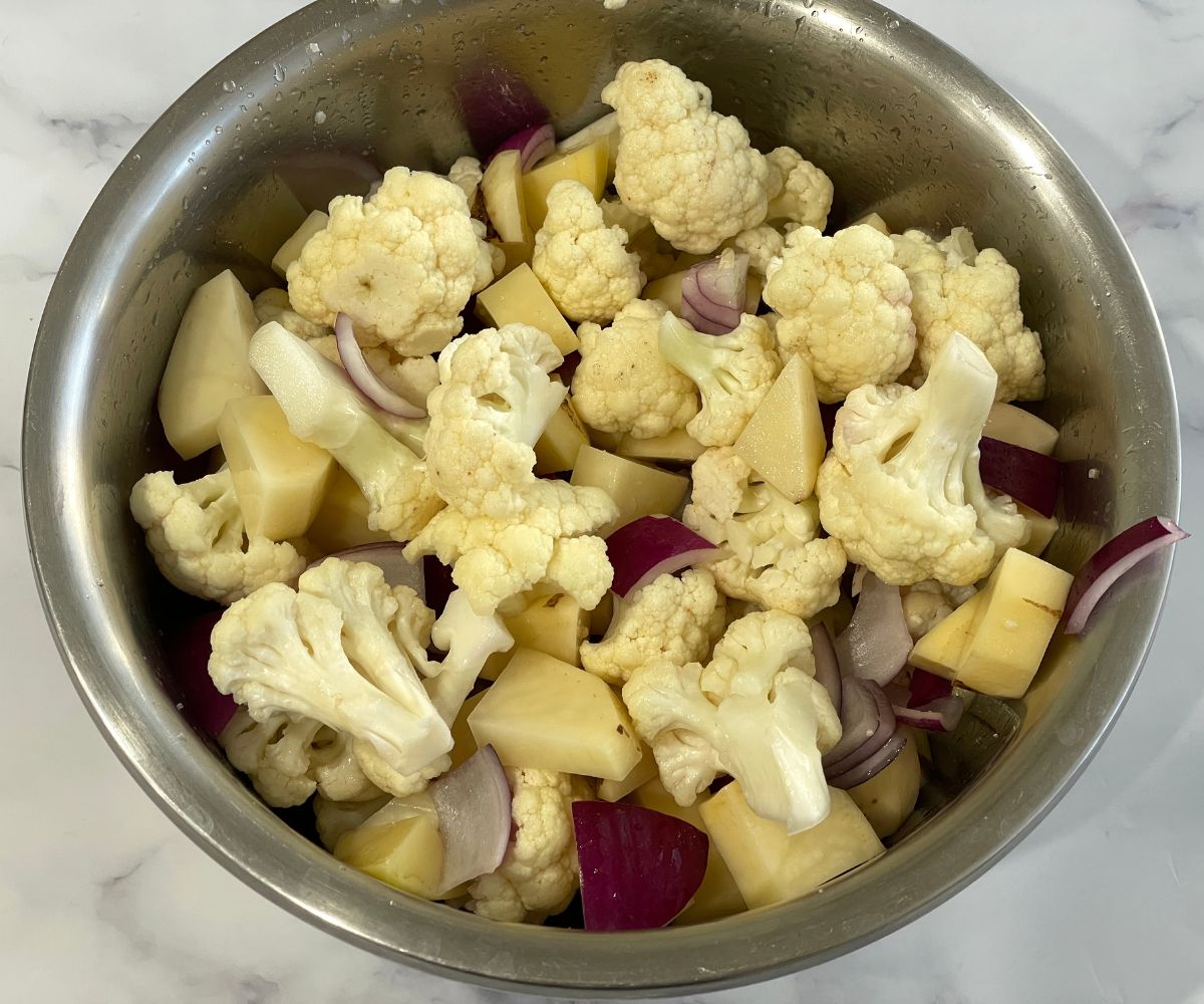 A bowl is with cauliflower, potato cubes and chopped onions.