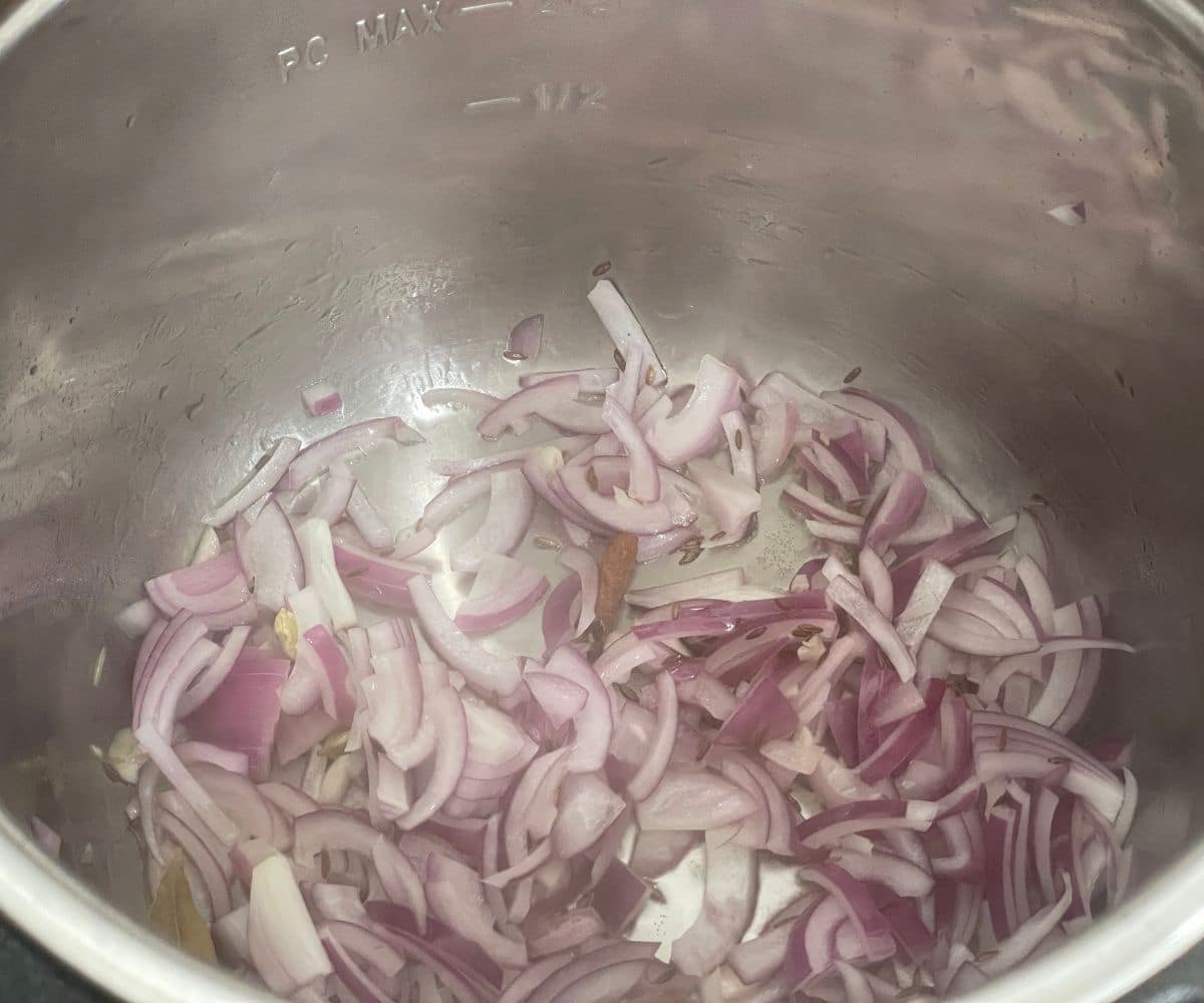 A pot is with spices and chopped onions on the heat.