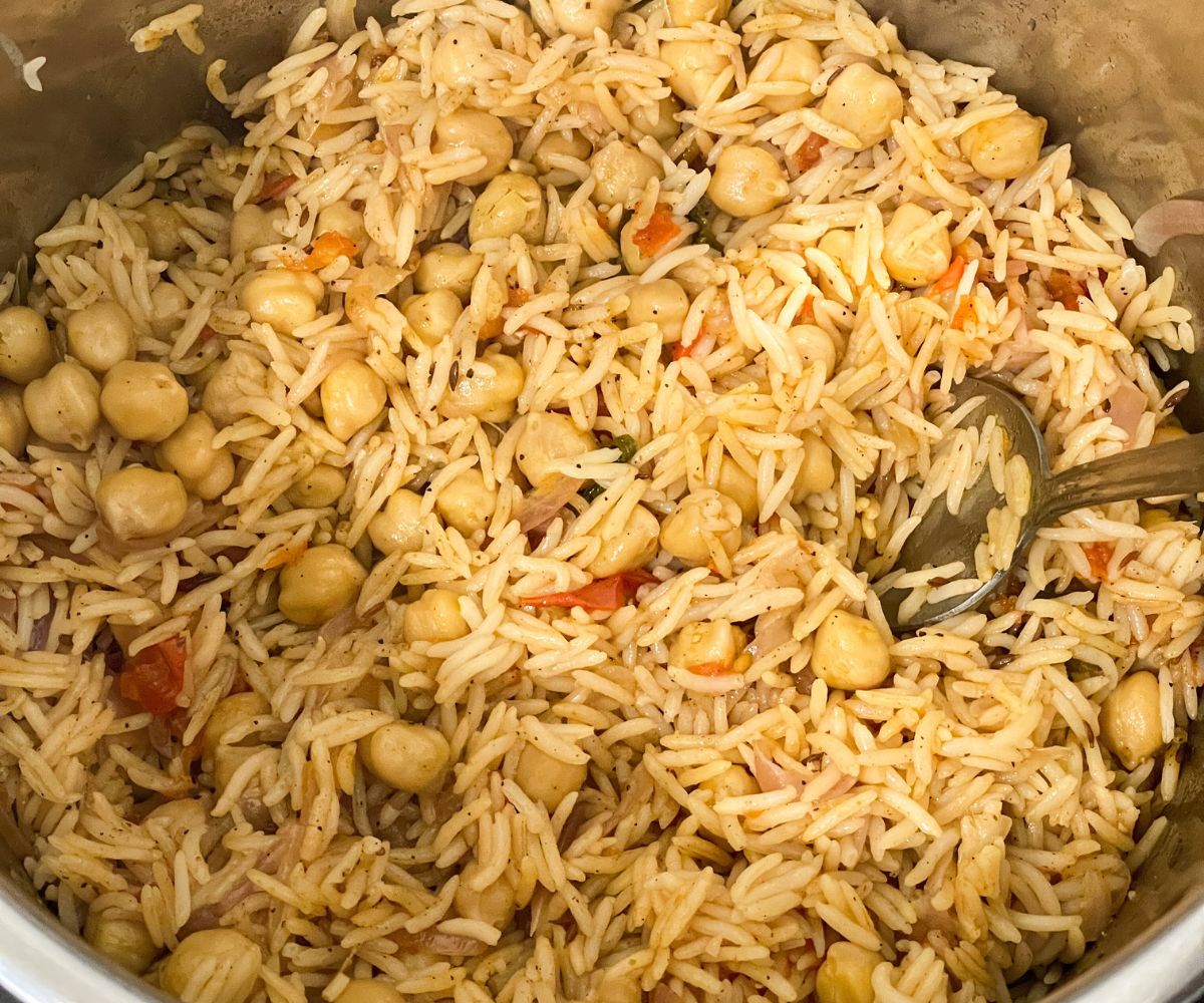 A pot of chana pulao is on the surface with spoon inserted.